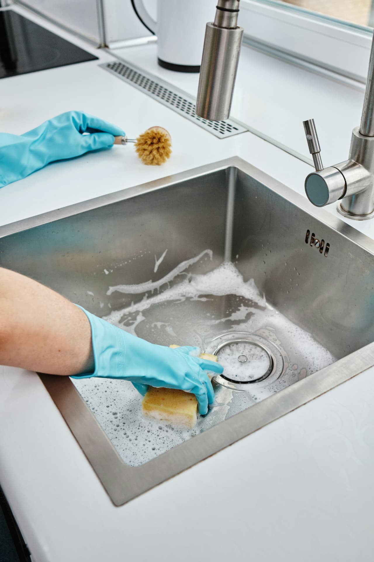 Gloved hands scrubbing a stainless steel kitchen sink